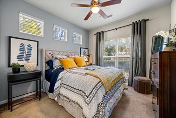 A bedroom with a bed, a ceiling fan, and a window with blinds.